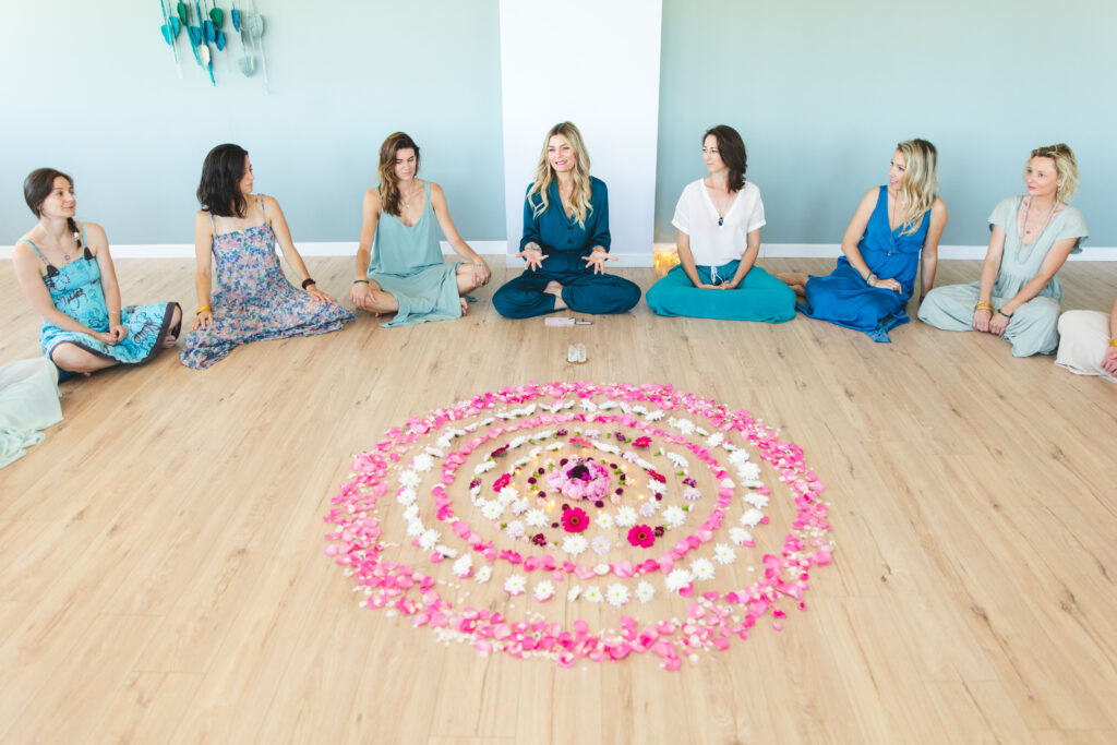 femmes réunies dans un cercle de parole autour 'un mandala de fleurs roses et blancs